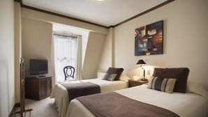 Quarto de hotel com duas camas, televisão, escrivaninha e um quadro na parede.