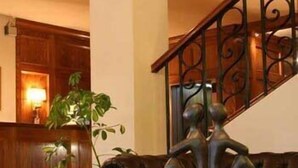 Um saguão com balcão de madeira, planta em vaso, grade metálica decorativa e sofá de couro marrom.