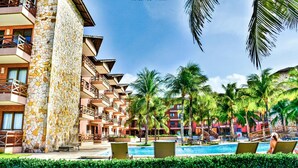 Un hotel con fachada de piedra, varios balcones, piscina y palmeras.