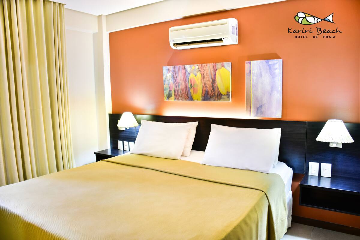 Habitación de hotel con cama, dos mesitas de noche, aire acondicionado y una obra de arte en la pared.