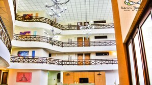 Un vestíbulo de hotel de varios niveles con un diseño moderno, que cuenta con un área de estar central, una araña y obras de arte en las paredes.