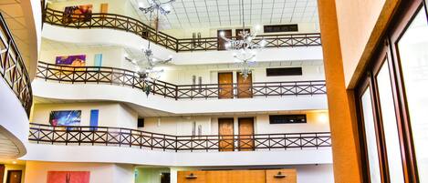 A multi-level hotel lobby with a modern design, featuring a central seating area, a chandelier, and artwork on the walls.