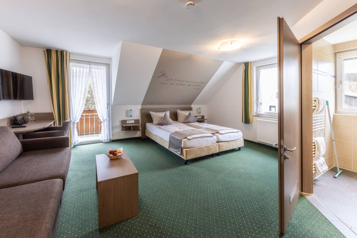 A hotel room with a bed, a sofa, a desk, a TV, and a balcony with curtains.