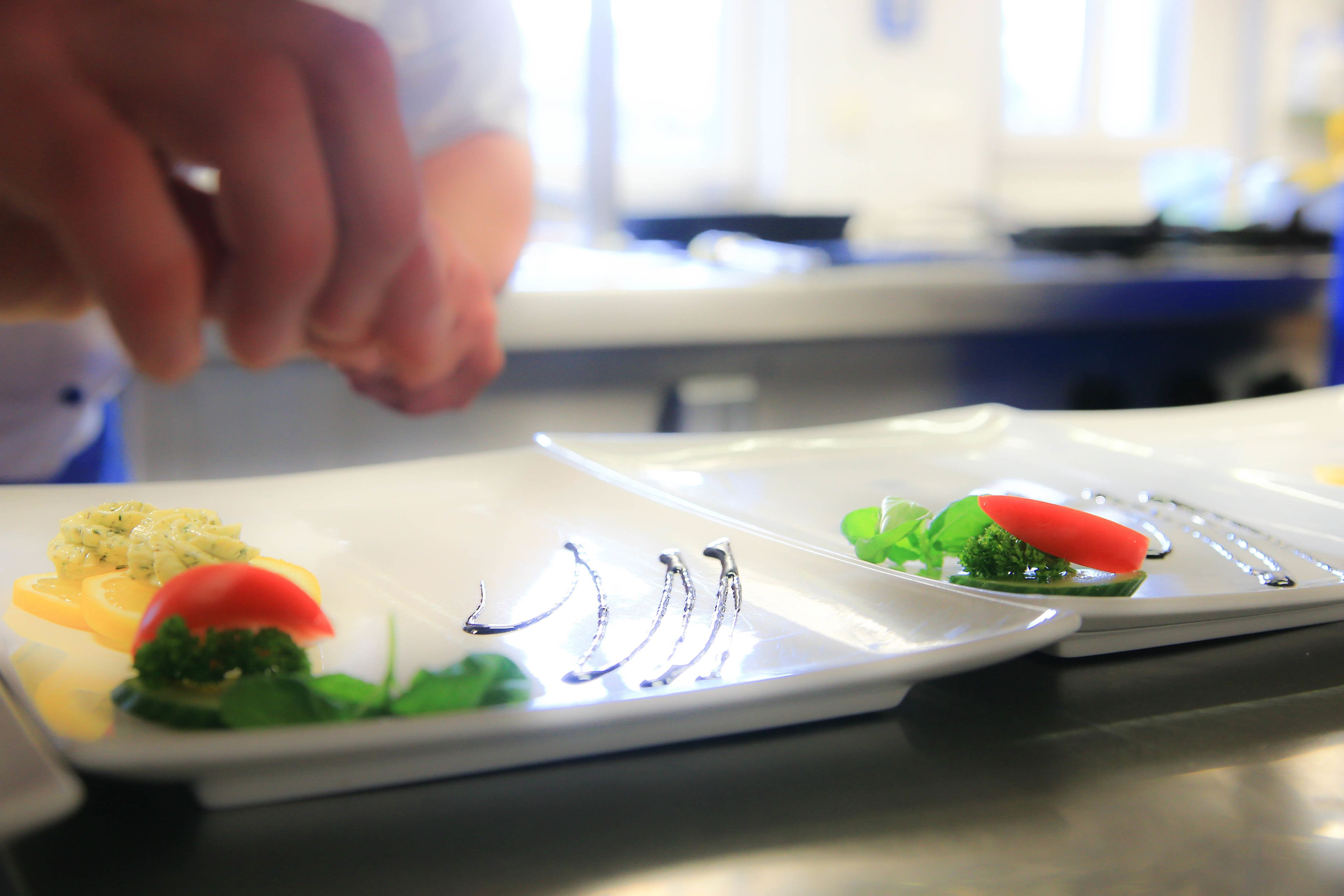 A chef's hand holding a utensil over a dish with various food items.