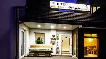 A hotel entrance with a wooden bench outside, a welcome sign, and a visible door.