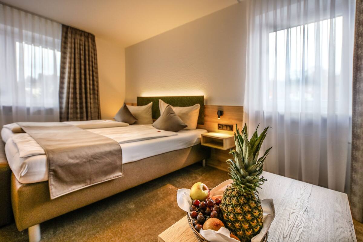 A hotel room with a bed, a nightstand, and a table with a fruit bowl.