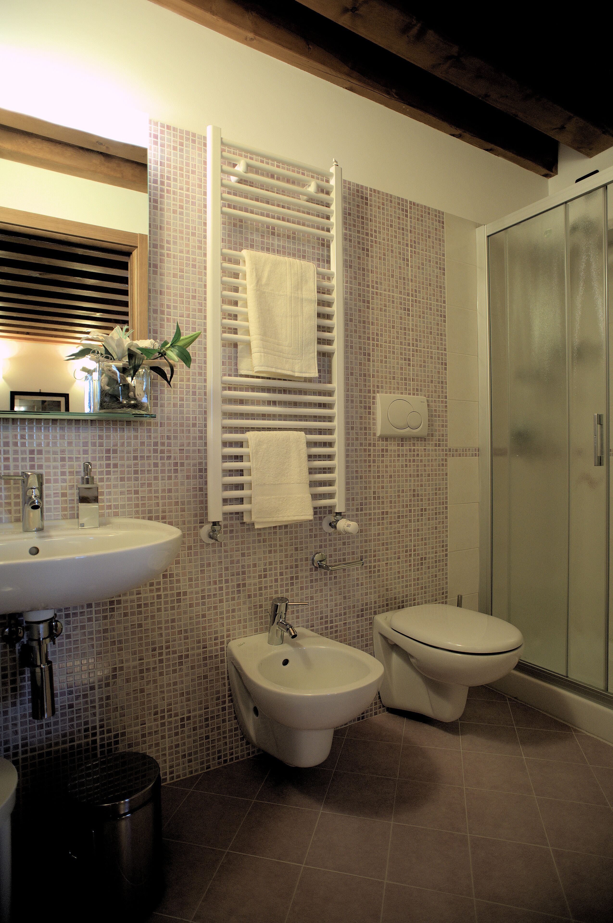 Ein Badezimmer mit Waschbecken, Bidet und Toilette, geflieste Wände und einer Duschkabine aus Glas.