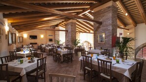 Un restaurante espacioso con varias mesas y sillas, vigas de madera en el techo y una pared de ladrillo.