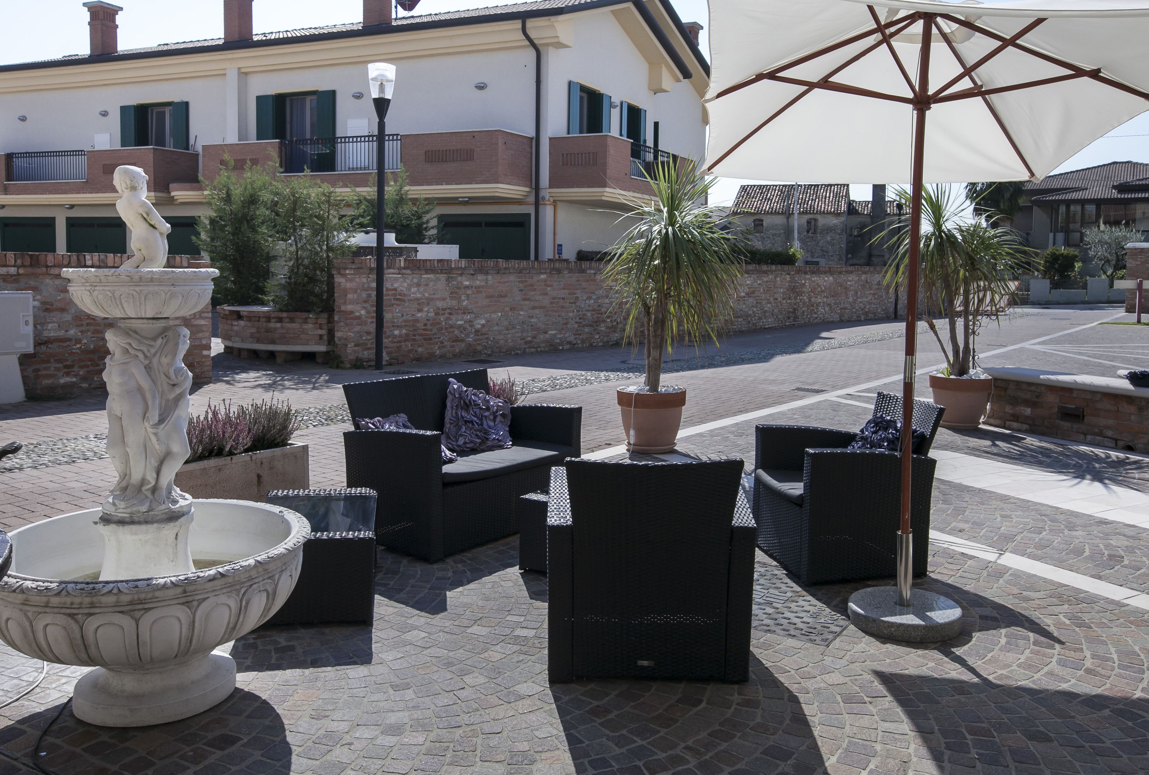Un espacio al aire libre con mobiliario de mimbre, una fuente de piedra y plantas en macetas.