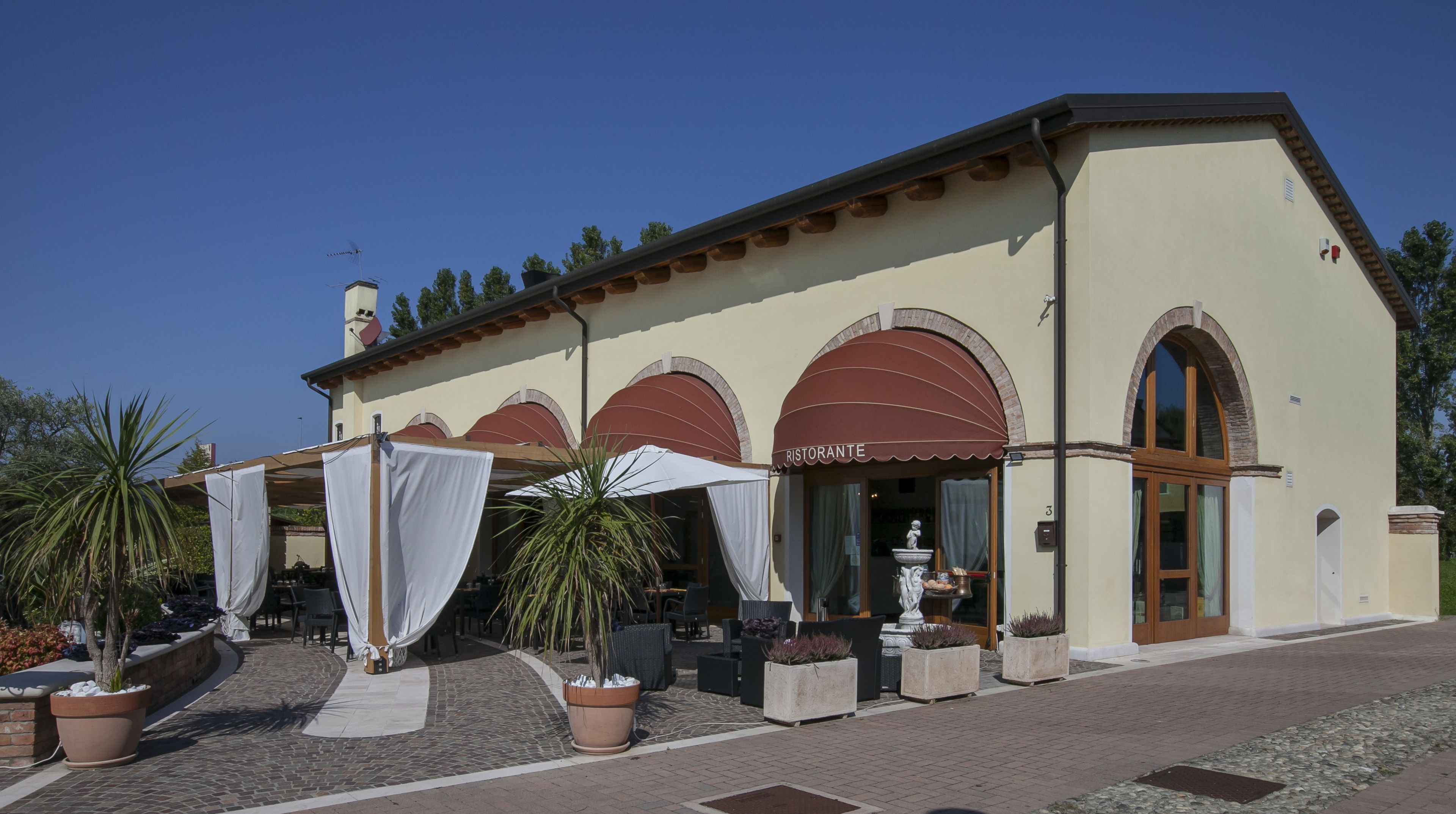 A building with a restaurant named "Ristorante" featuring outdoor seating with umbrellas and potted plants.