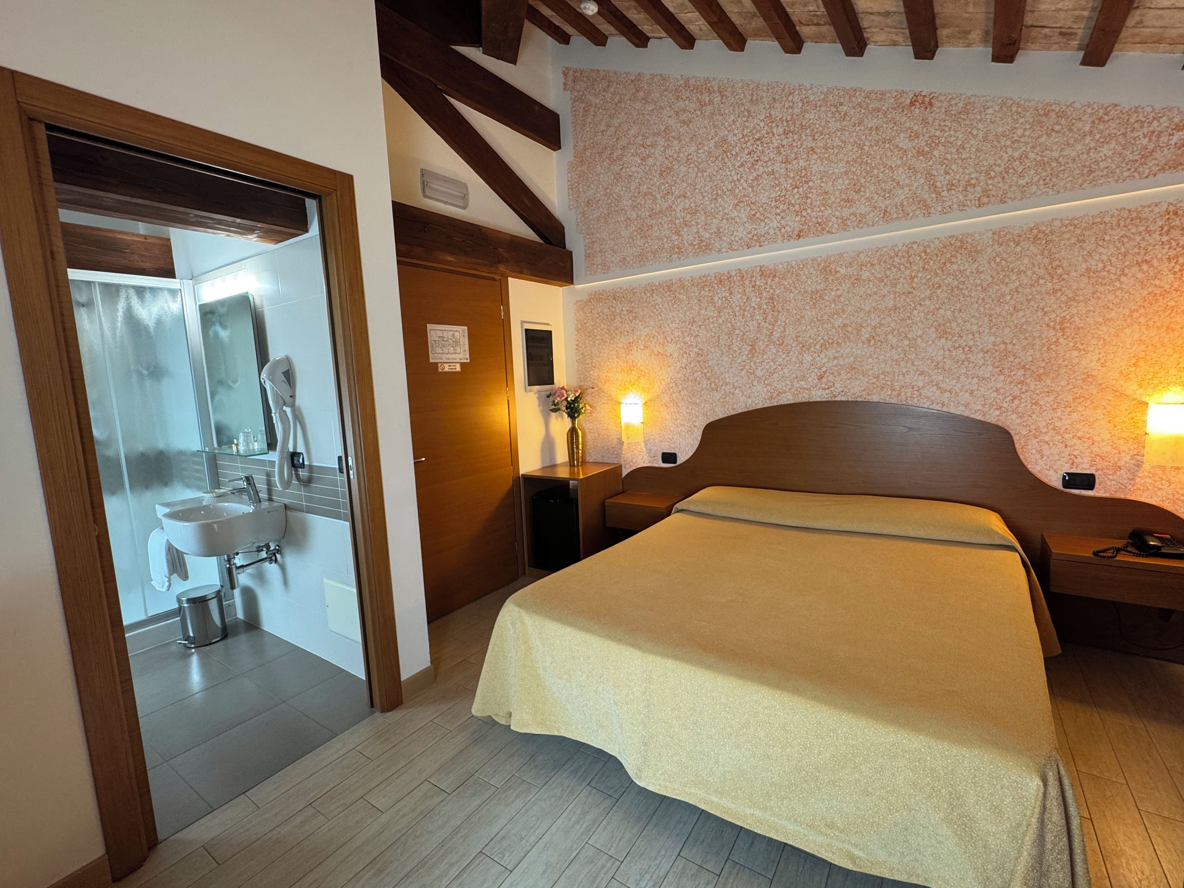 Ein Schlafzimmer mit Bett, Nachttischen, einer Wandlampe und einem durchgegangenen Tür sichtbaren Badezimmer.