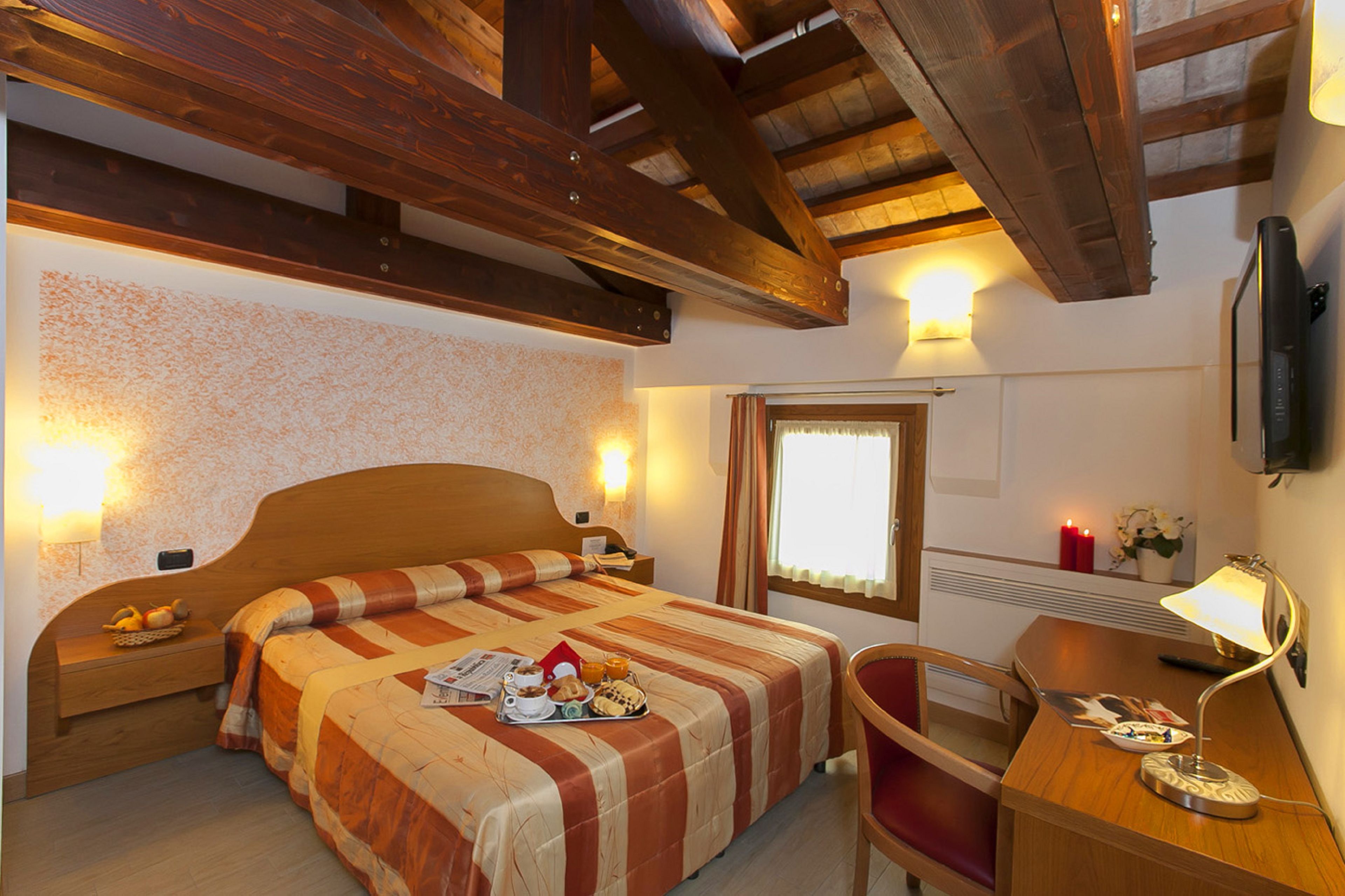 Habitación de hotel con cama de madera, un escritorio, una silla, un ventanal y un televisor de pantalla plana.
