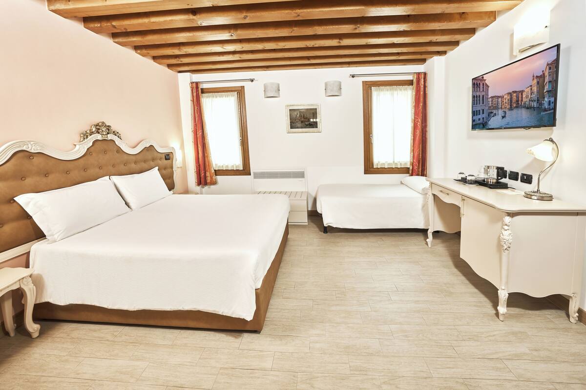 A bedroom with a large bed, a smaller bed, a desk, and a television.
