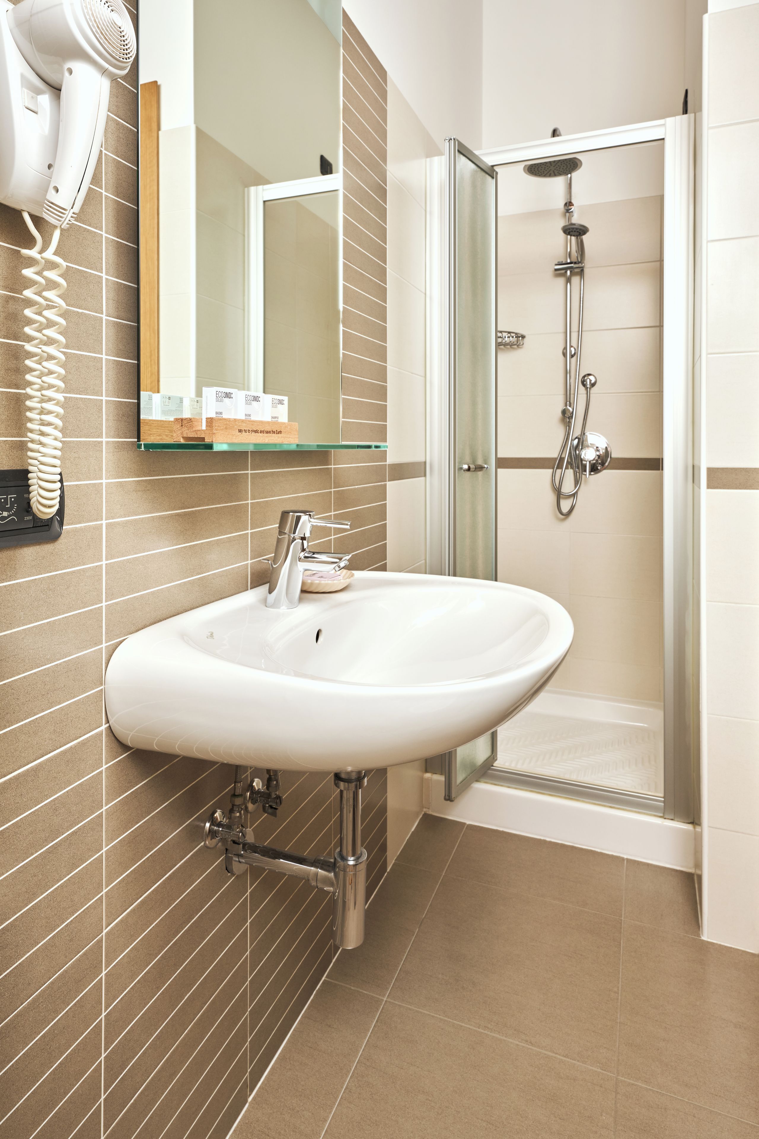 Ein Badezimmer mit Waschbecken, Duschkabine aus Glas und einem an der Wand befestigten Föhn.