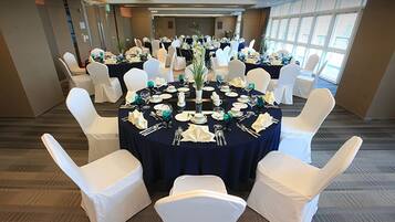 A conference room with round tables set for a formal event, white chairs, and a large window providing natural light.