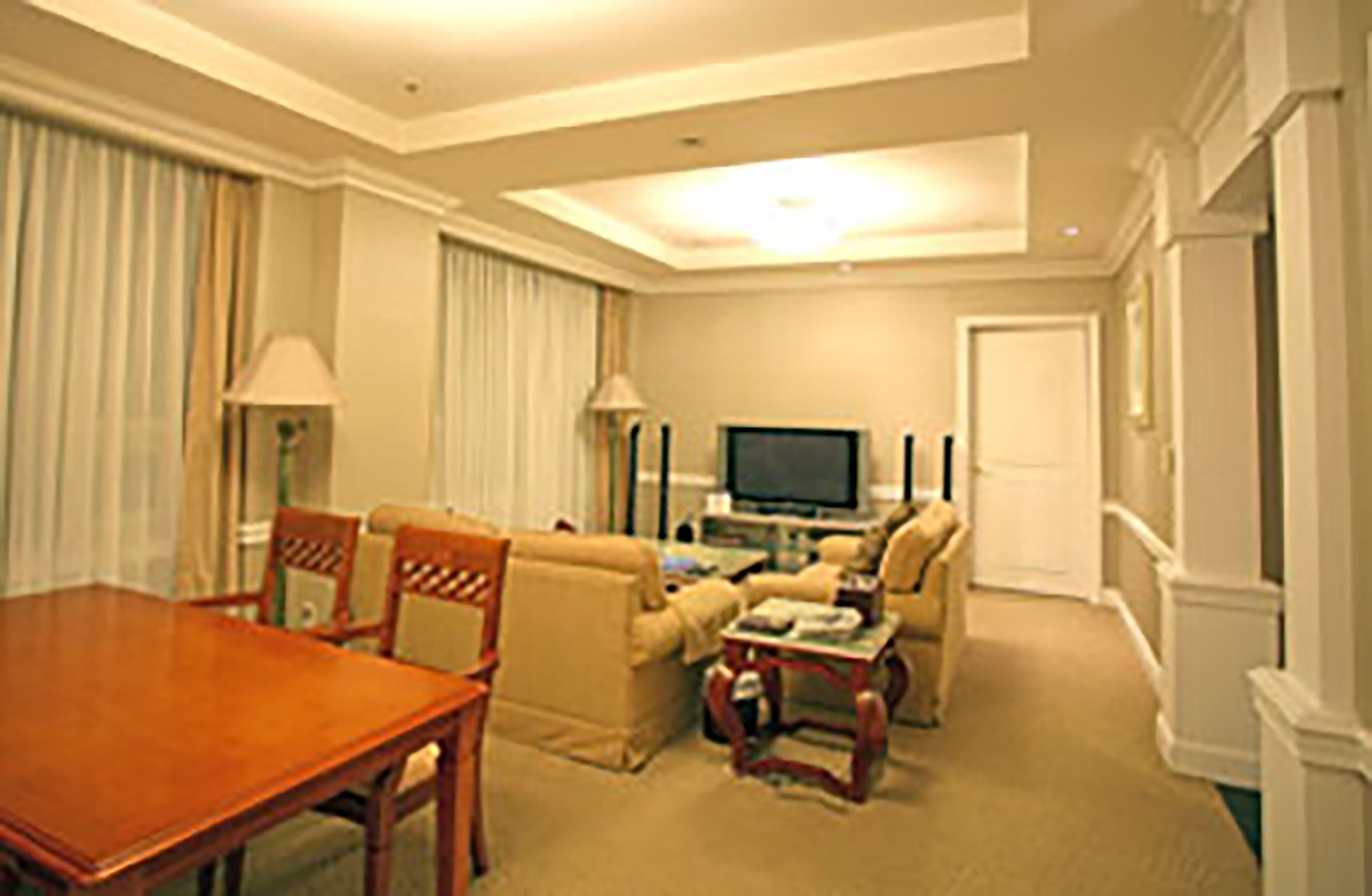A hotel room with a wooden dining table, beige sofas, a flat-screen TV, and a small coffee table.