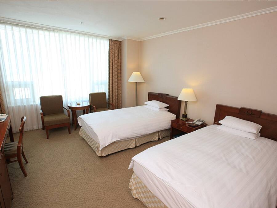 A hotel room with two beds, a desk with a chair, a small table, and a lamp.