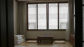 A room with a tatami mat floor, a low wooden table, and a window with vertical blinds.