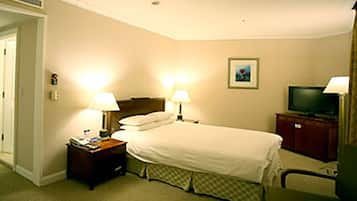 A hotel room with a bed, two bedside lamps, a television, and a small table with a lamp.