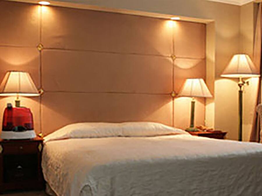 Habitación de hotel con una cama grande, dos mesitas de noche con lámparas, una silla y cabecera con iluminación integrada.