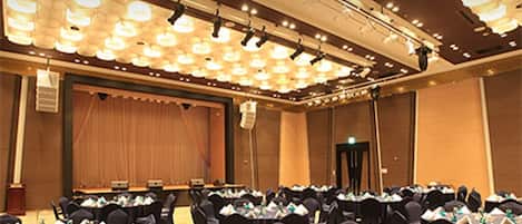 Un salón de conferencias con mesas redondas, sillas negras y un escenario con cortinas.