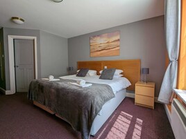 Habitación de hotel ordenada con cama, mesita de noche, un cuadro en la pared y una puerta.