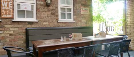 An outdoor seating area with a wooden table and chairs, a brick wall, and a sign indicating a non-smoking area.