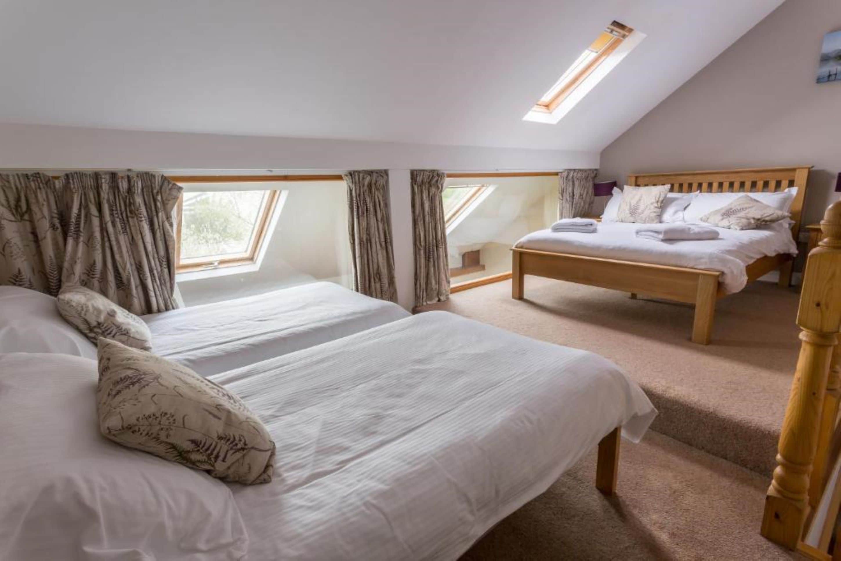 A bedroom with two beds, a wooden headboard, and a skylight.