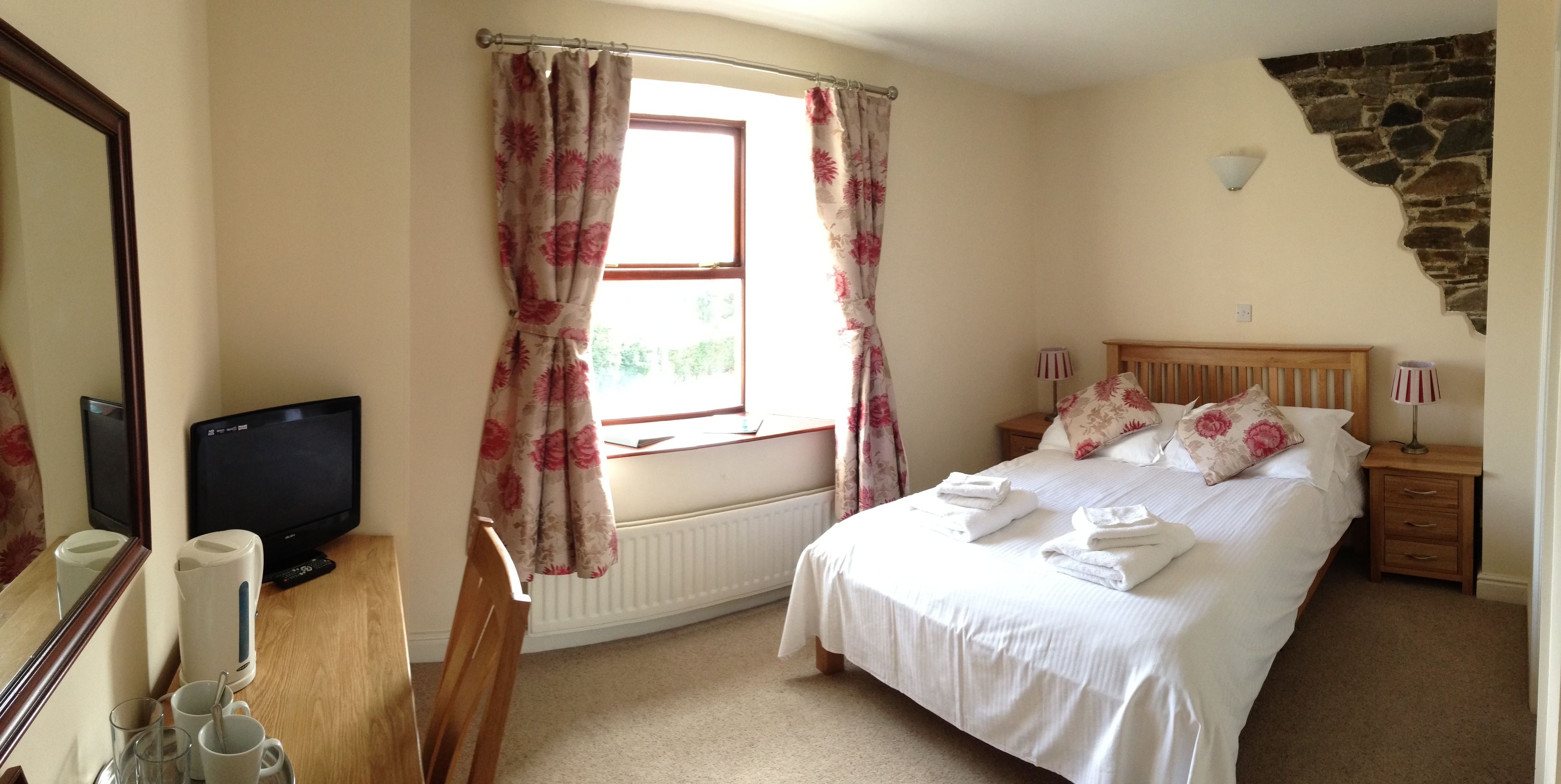 A bedroom with a bed, a television, a window with curtains, a nightstand, and a lamp.