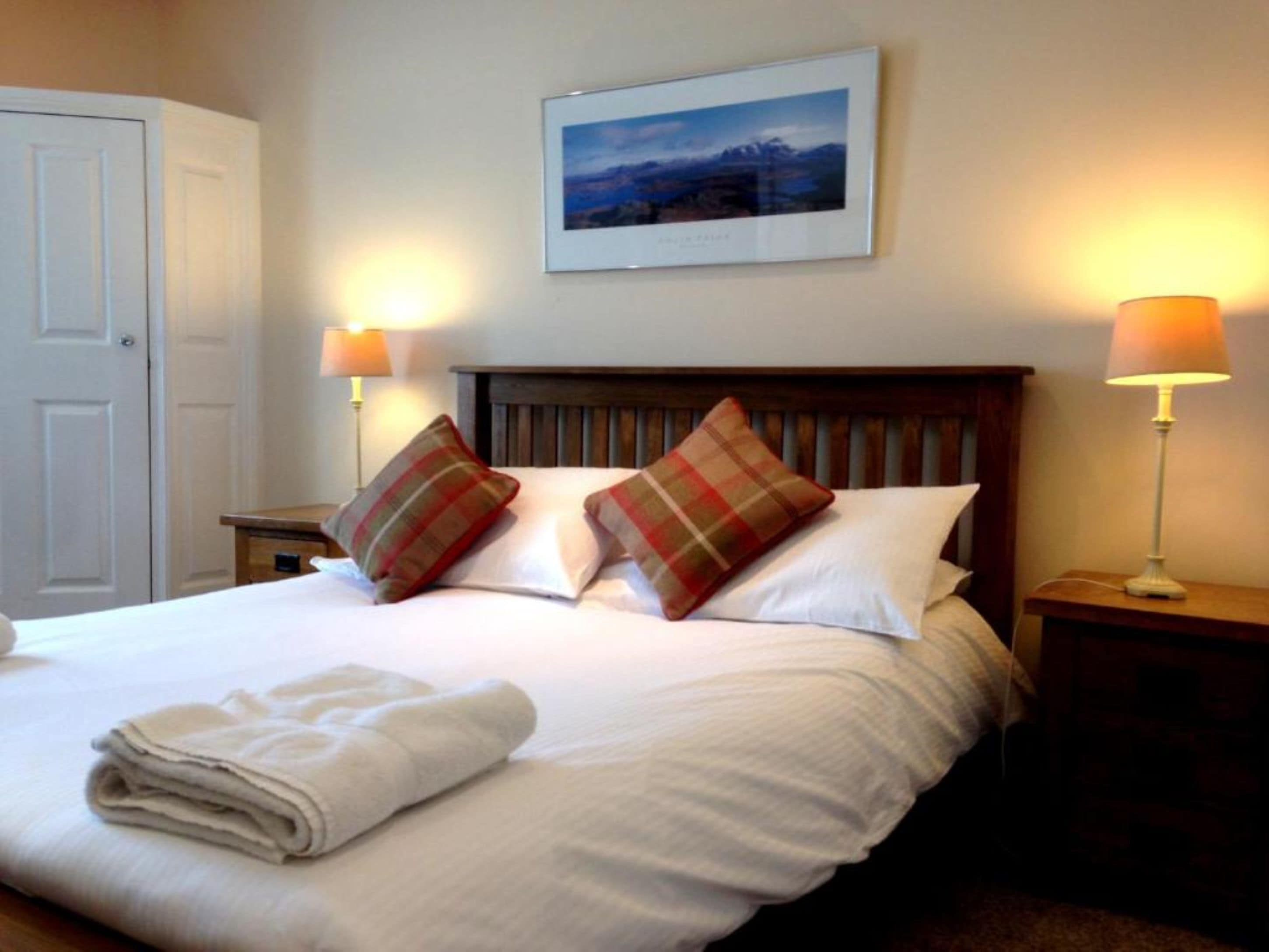 A neatly made bed with plaid pillows, a folded towel, and two bedside lamps.