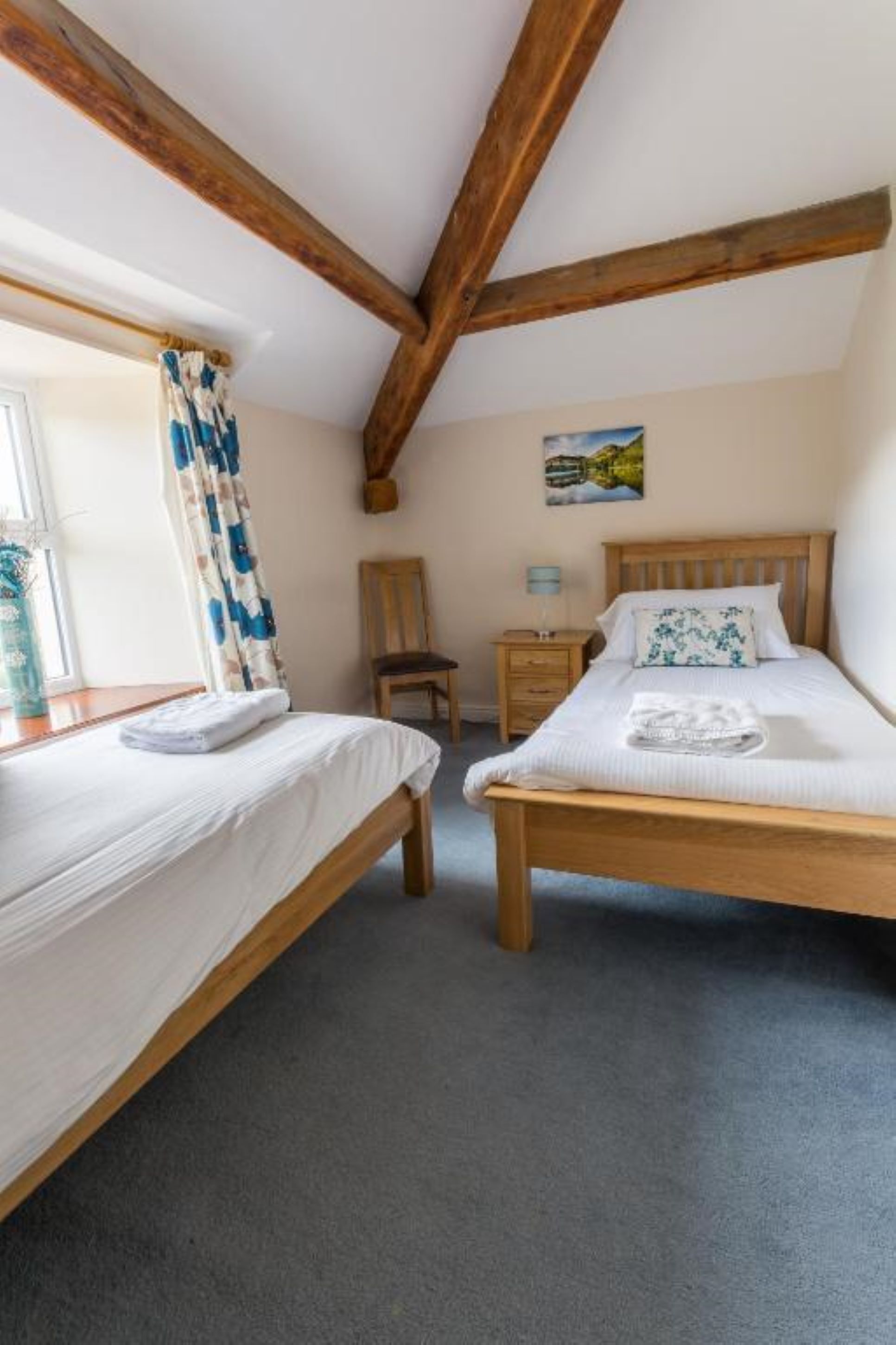 A bedroom with two wooden beds, a chair, a nightstand, and a window with curtains.
