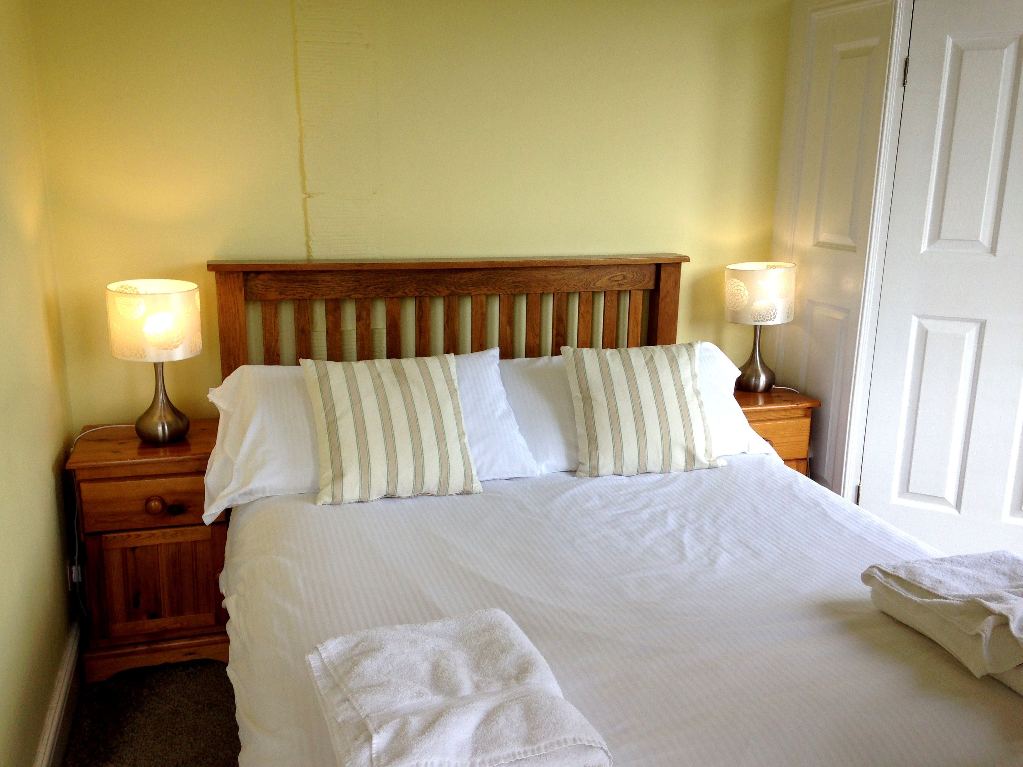 Una cama bien hecha con almohadas a rayas, un cabecero de madera y dos lámparas de noche.