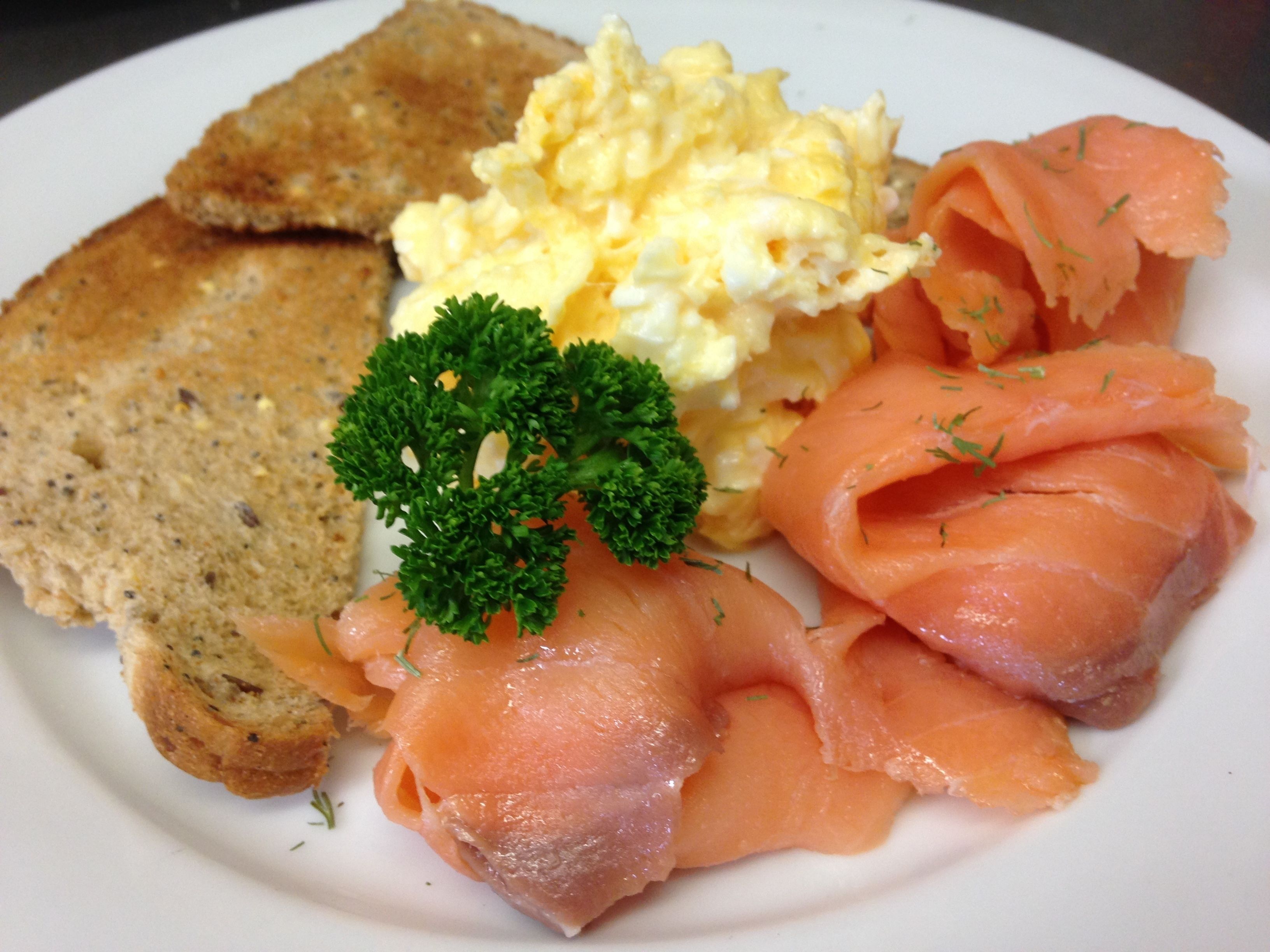 A plate with smoked salmon, scrambled eggs, toast, and a sprig of parsley.