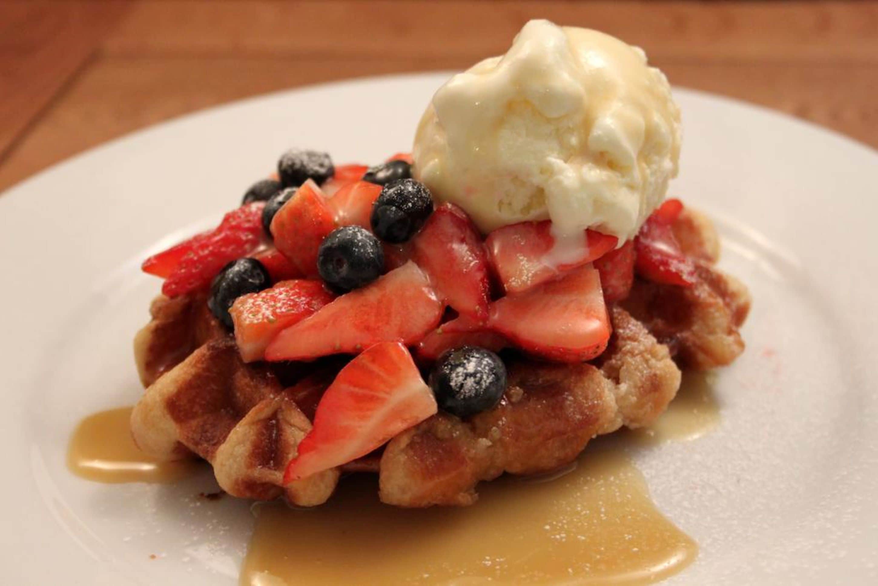 A plate of waffles topped with strawberries, blueberries, and a scoop of vanilla ice cream, with syrup drizzled over.