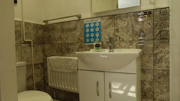 A bathroom with a white toilet, a sink with a soap dispenser, a towel rack, and a poster with COVID-19 guidelines.