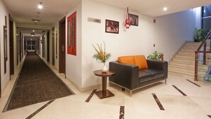 A hotel lobby with a long hallway, a sofa, a small table with a vase, and a staircase. - Hotel Trinity Isle (Bengaluru)
