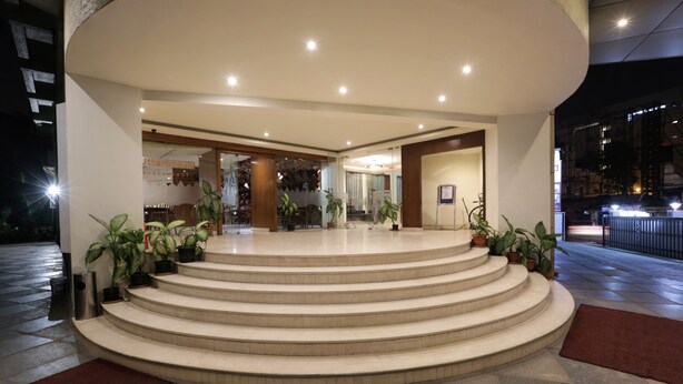 A hotel entrance with a curved staircase leading to the lobby, surrounded by potted plants and a red carpet. - Hotel Trinity Isle (Bengaluru)
