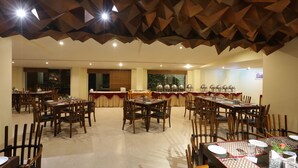 A dining area with multiple tables and chairs, a patterned table runner, and a ceiling with geometric wooden panels. - Hotel Trinity Isle (Bengaluru)