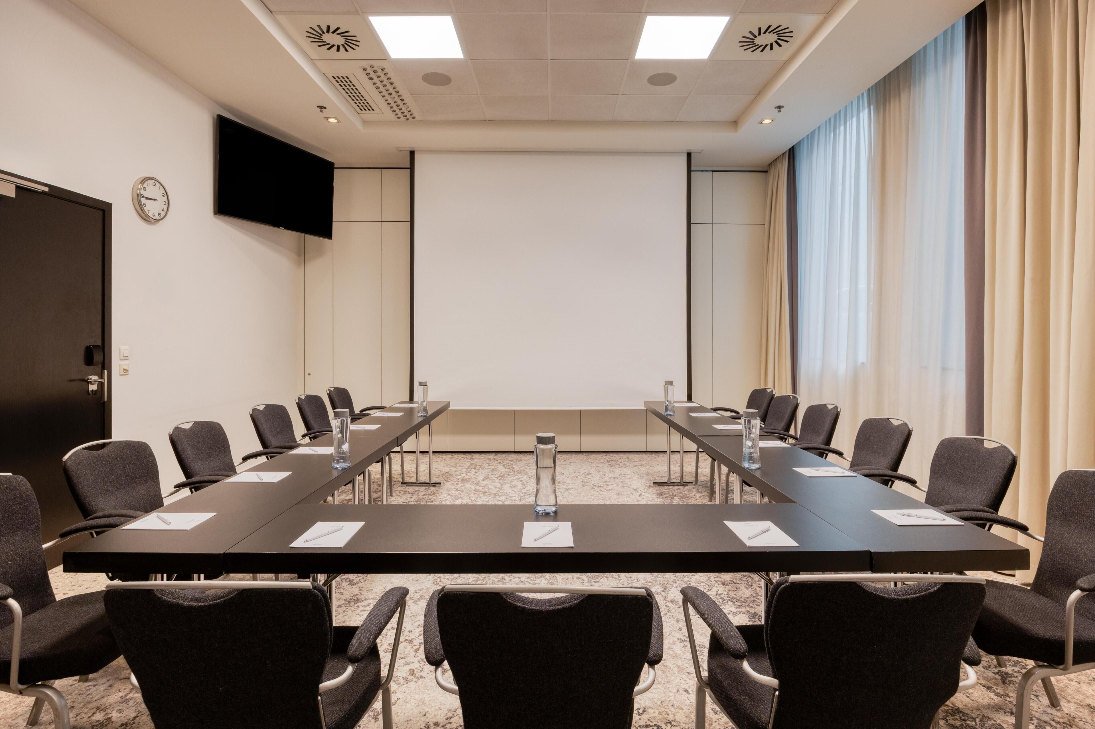 A conference room with a long table, chairs, a clock, a TV, and a projector screen.