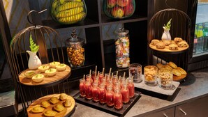 Un bufé con diversos alimentos y bebidas, que incluye cestas de fruta, pasteles y una variedad de refrescos.