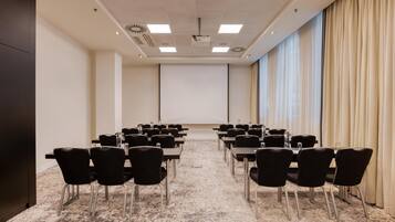 A conference room with a long table, chairs, a projector screen, and a large window with curtains.