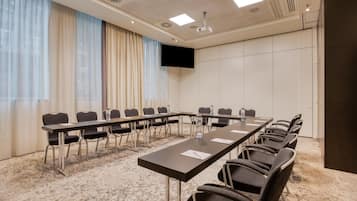 Une salle de conférence équipée d’une longue table, de chaises, d’un téléviseur à écran plat et d’un projecteur au plafond.