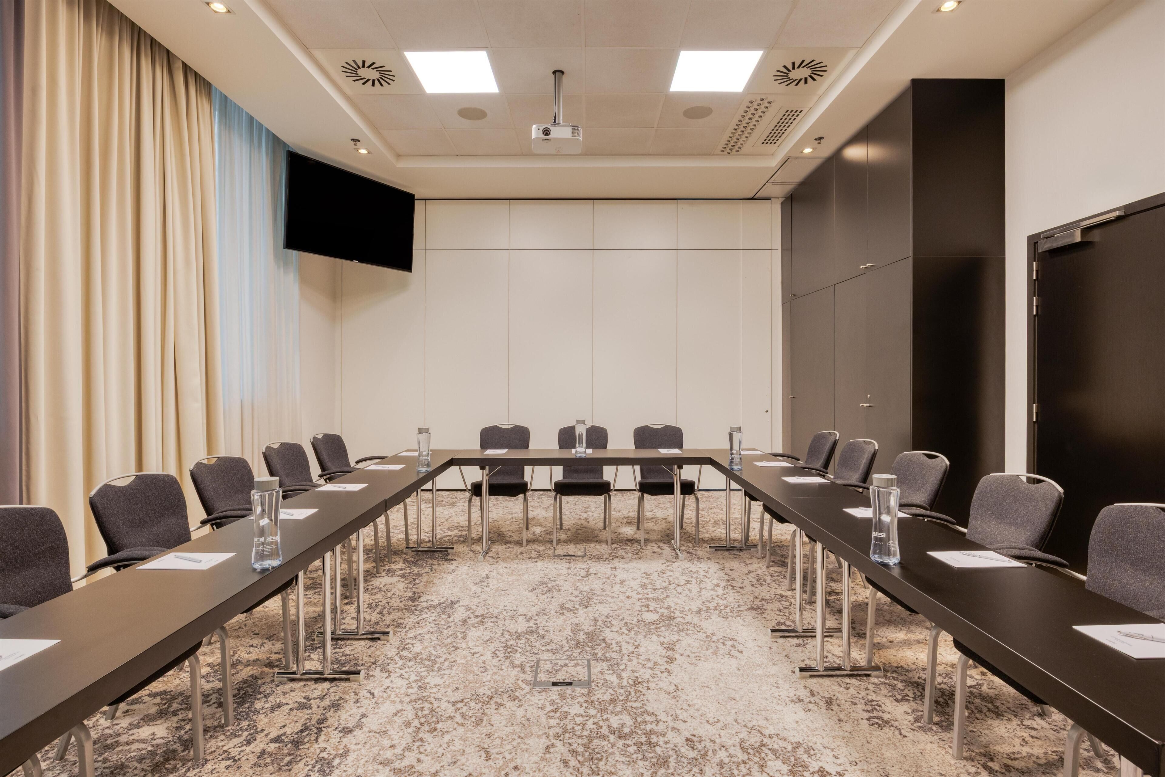 Une salle de conférence équipée d’une longue table, de chaises, d’un projecteur et d’un écran.