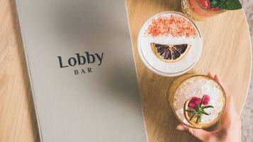 Una mesa redonda de madera con un menú que dice "Lobby Bar" y dos bebidas adornadas.