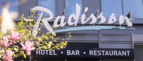 A building with a sign that reads 'Radissen' and a lower sign indicating 'HOTEL • BAR • RESTAURANT'.