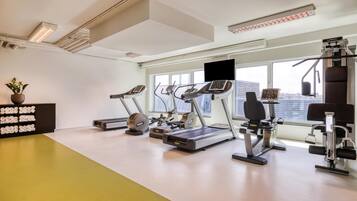 A modern gym with various exercise equipment, large windows, and a potted plant.