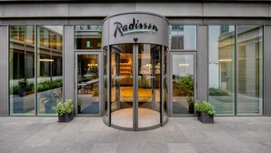 Entrada de un hotel Radisson con puerta giratoria, amplios ventanales y plantas en macetas.
