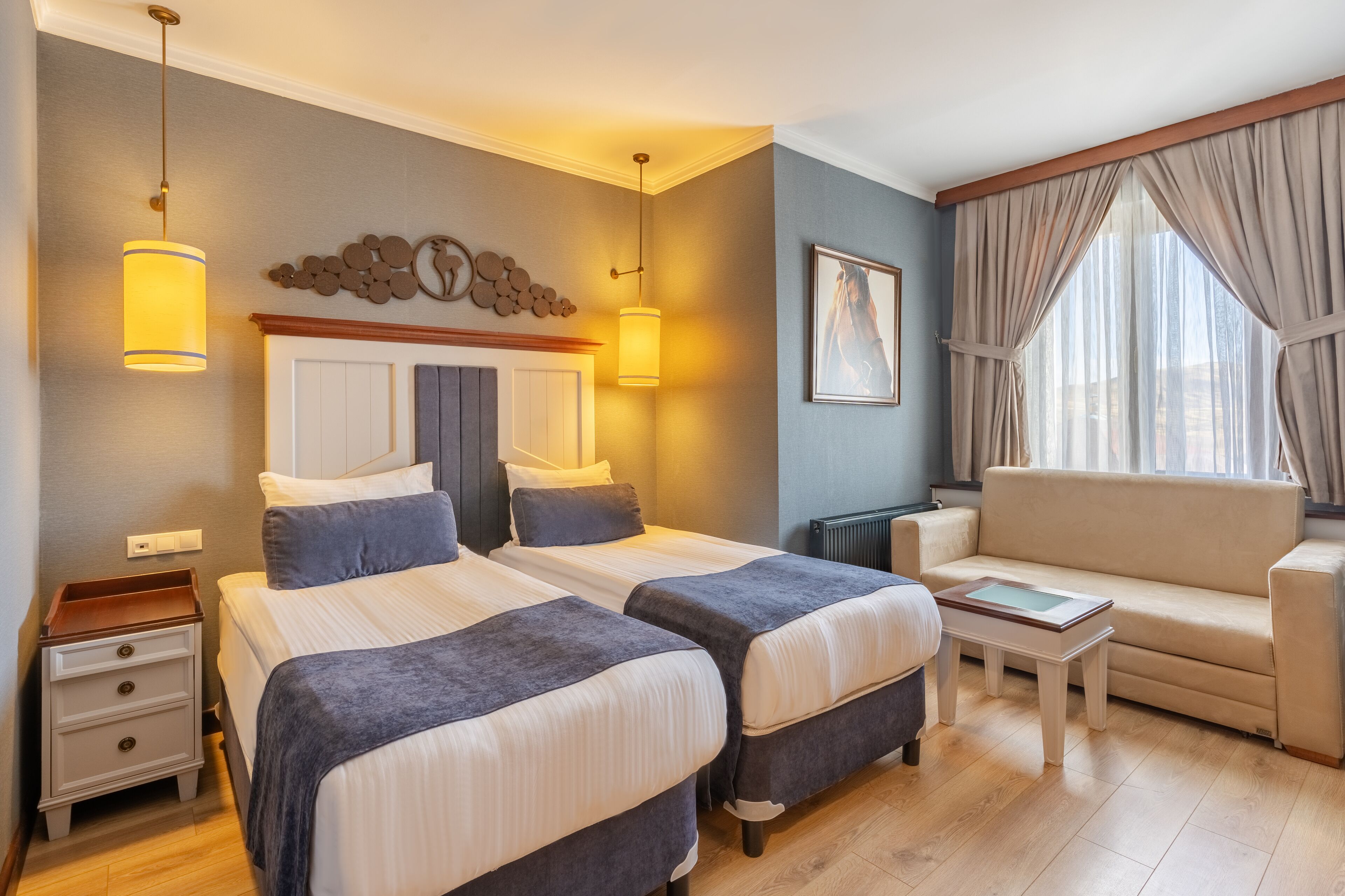 Una habitación de hotel con dos camas, un sofá, una mesita y una ventana con cortinas.