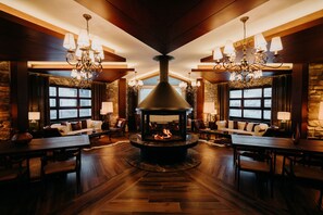 A cozy interior with a central fireplace, wooden floors, stone walls, and multiple seating areas. - Mirada Del Lago Hotel (Kayseri)
