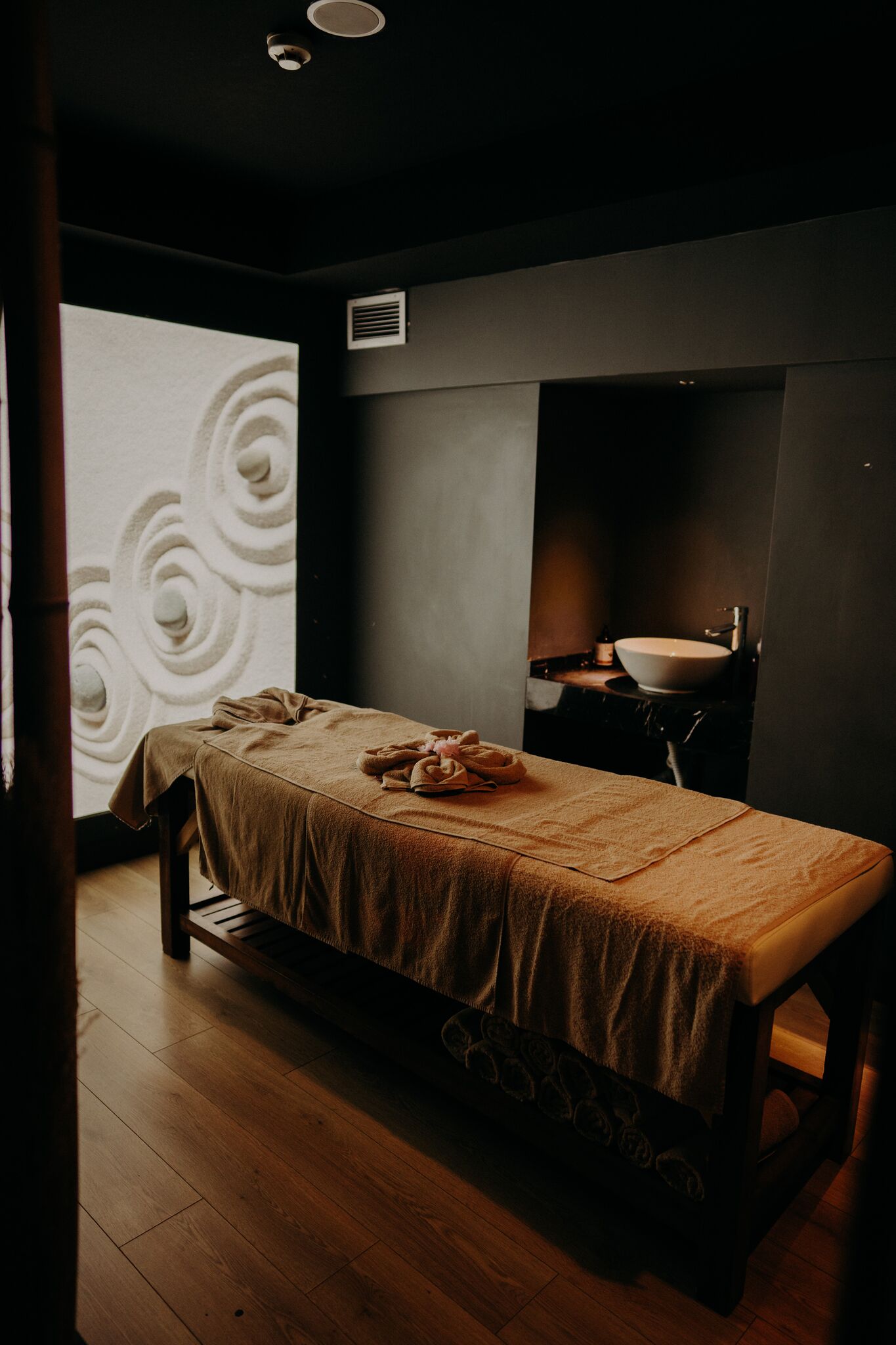 A room with a bed, a sink, and a large wall with a swirl pattern.